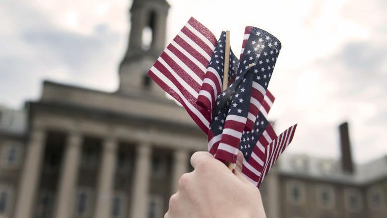 A person holds a group of mini American flags in front of the Old Main building on Penn State's University Park campus.